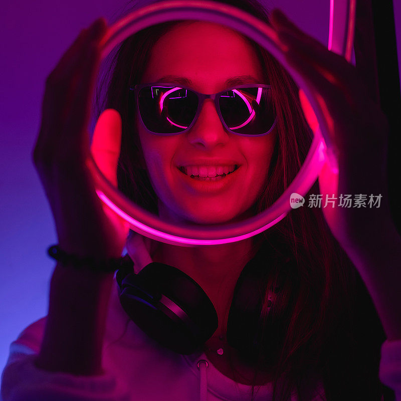 Female portrait in neon light. Fashion woman in purple color. Vibrant background at the studio. Futuristic concept. Girl wear sunglasses and hoodie with bluetooth wireless headphones